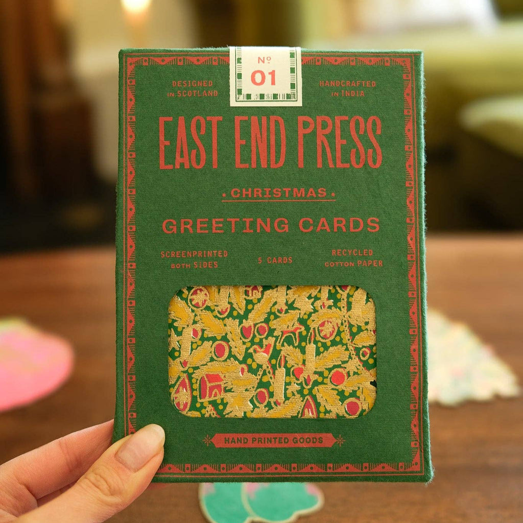 Green box of East End Press Christmas greeting cards held by a hand on a wooden surface.