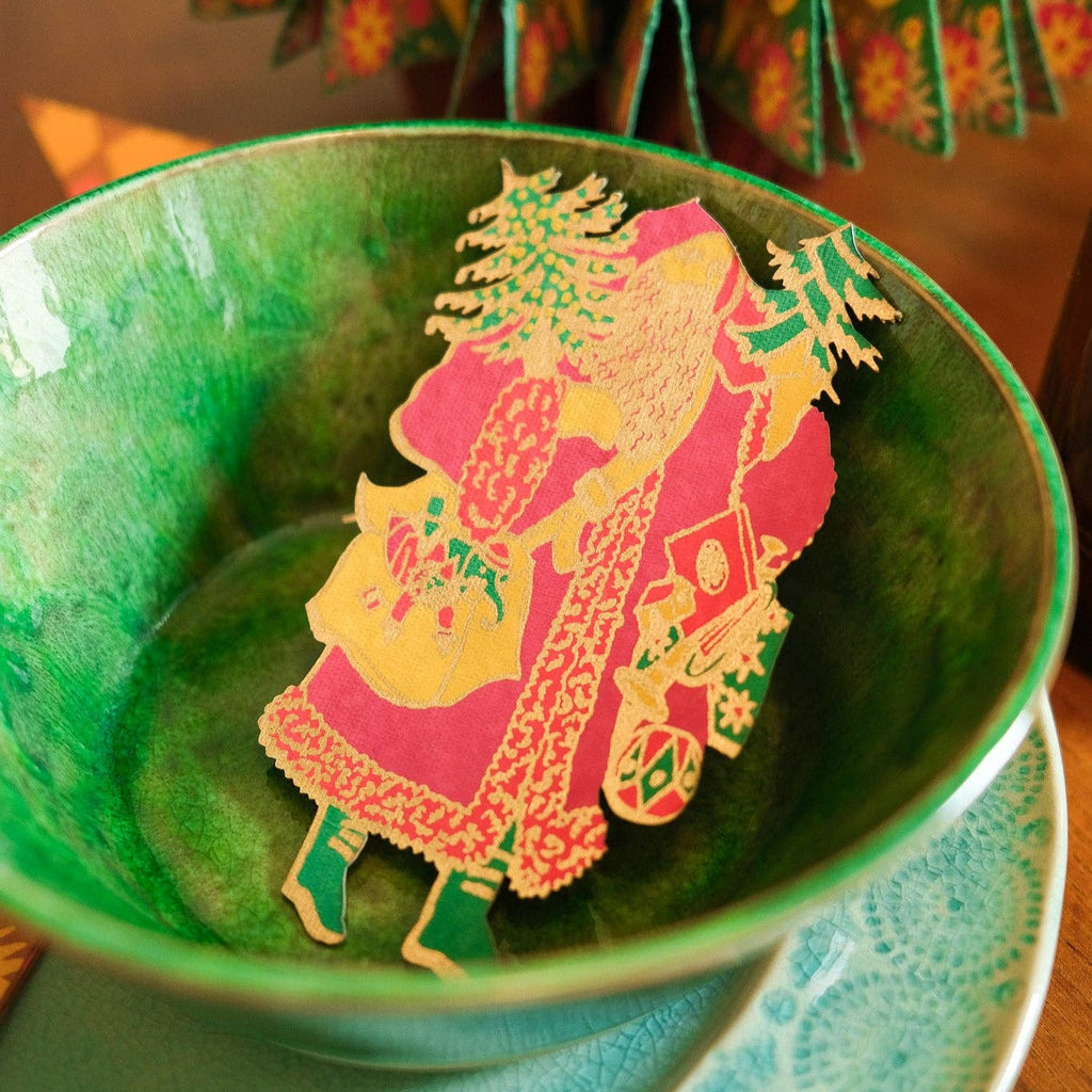 Decorative paper cutout of a woman with a child in a green bowl on a wooden surface.