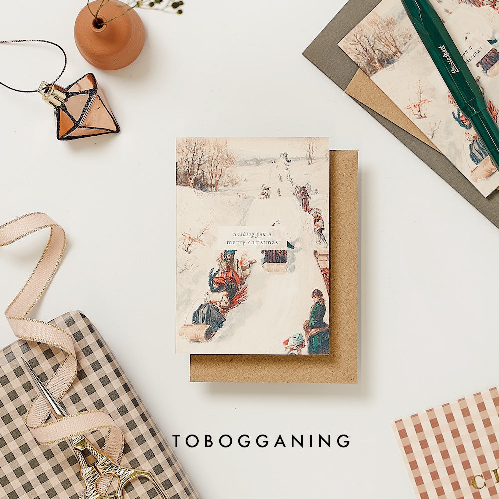 Christmas card with Tobogganing design on a white surface with decorative items.