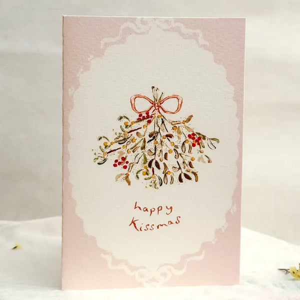 Greeting card with mistletoe design and 'happy Kissmas' text on a pink background