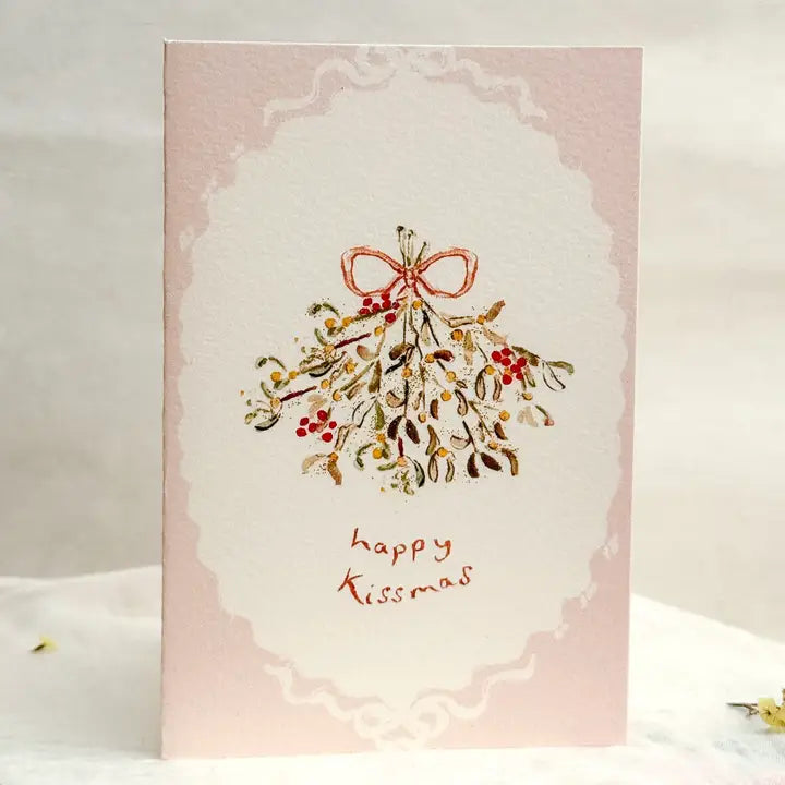 Greeting card with mistletoe design and 'happy Kissmas' text on a pink background