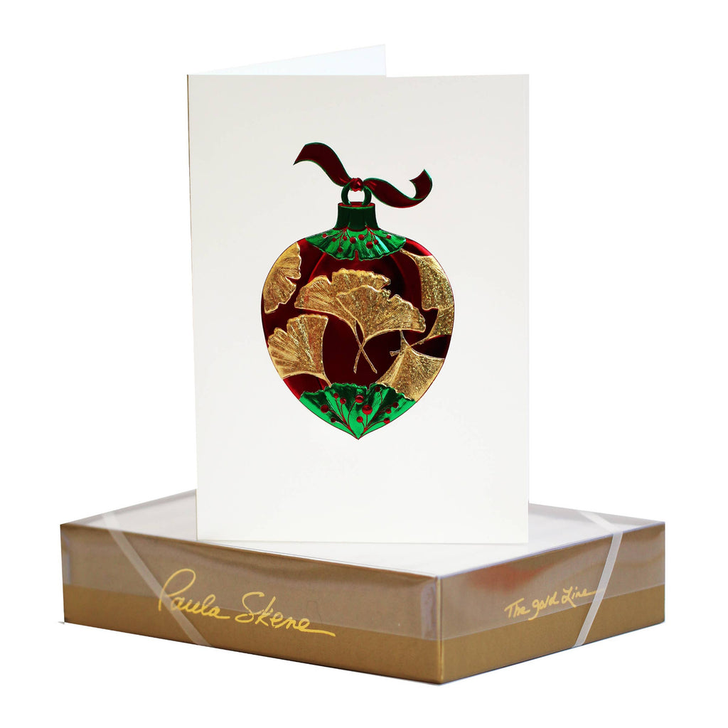 Decorative heart-shaped ornament with gold and green design on a white card, placed on a branded box.