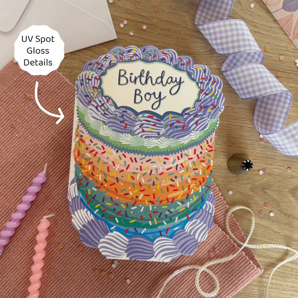 Colorful birthday cake card with 'Birthday Boy' text on a wooden surface.