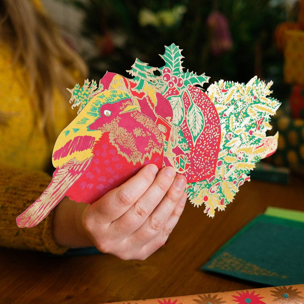 Person holding a colorful paper cutout of a bird with a floral design on a wooden surface.