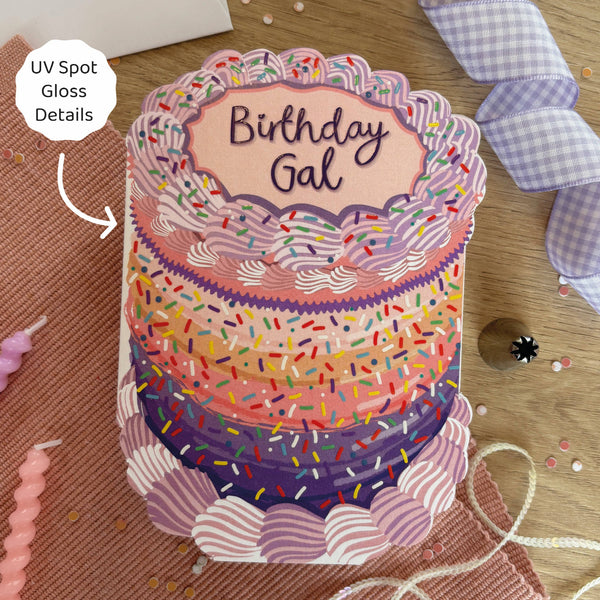 Decorative birthday card with a cake design and 'Birthday Gal' text on a wooden surface.