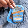 Blue decorative item resembling a sardine can with gold accents, held by a hand on a fluffy gray background.