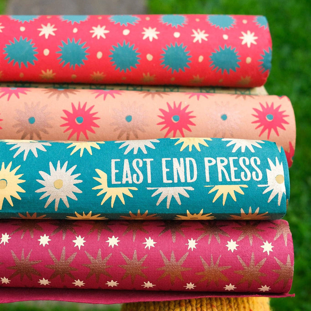 Stack of colorful fabric rolls with 'East End Press' branding on a grassy background