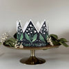 Decorative paper crown with green leaf pattern on a white background