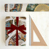 Gift wrapped in decorative paper with a red ribbon, next to a ruler on a white background