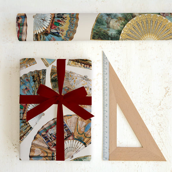 Gift wrapped in decorative paper with a red ribbon, next to a ruler on a white background