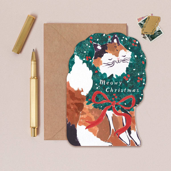 Cat-shaped Christmas card with 'Meowy Christmas' text, surrounded by a pen and envelope on a beige background.
