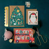 Three Christmas-themed greeting cards on a dark green surface with stationery items.