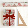 Gift wrapped in gingerbread house patterned paper with a red ribbon, next to a ruler on a white background.