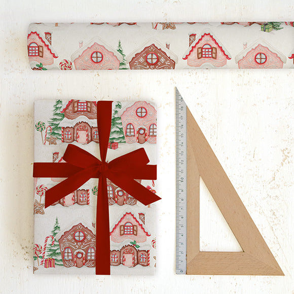 Gift wrapped in gingerbread house patterned paper with a red ribbon, next to a ruler on a white background.