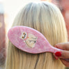 Person using a pink hairbrush with a cat design on a blurred background