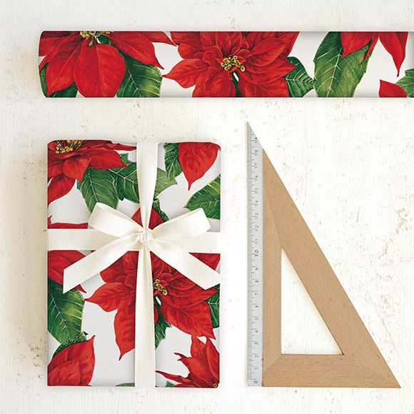Poinsettia-themed gift wrap with a wrapped present and a ruler for scale on a white background.