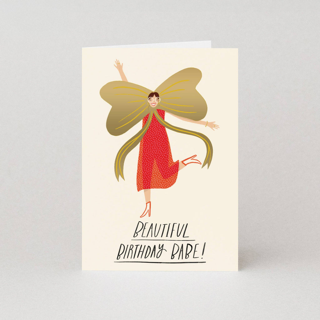 Greeting card with an illustration of a woman in a red dress with butterfly wings and text 'Beautiful Birthday Babe!' on a beige background.