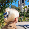 Person with blonde hair and blue hair accessory standing in front of Notre-Dame Cathedral