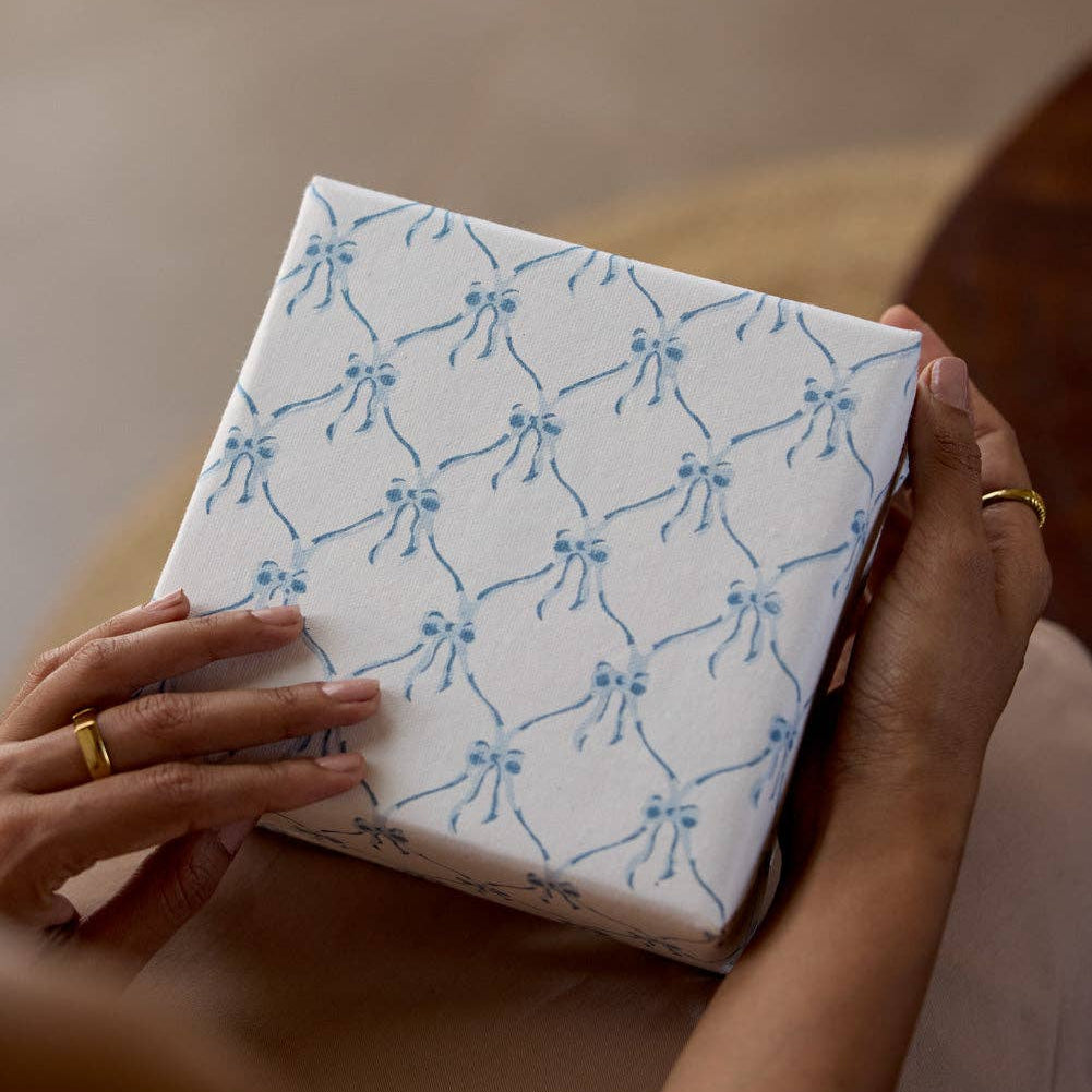 Person holding a box with blue bow pattern on a neutral background