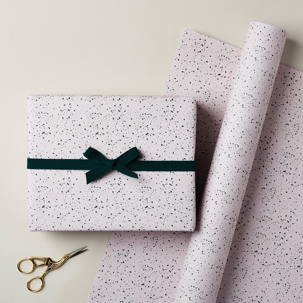 Speckled gift box with a green ribbon and scissors on speckled paper