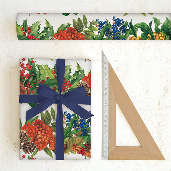 Christmas-themed wrapping paper with holly and berries, a wrapped gift with a blue ribbon, and a ruler on a white background.