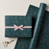 Green speckled gift box with a pink ribbon and scissors on a light background