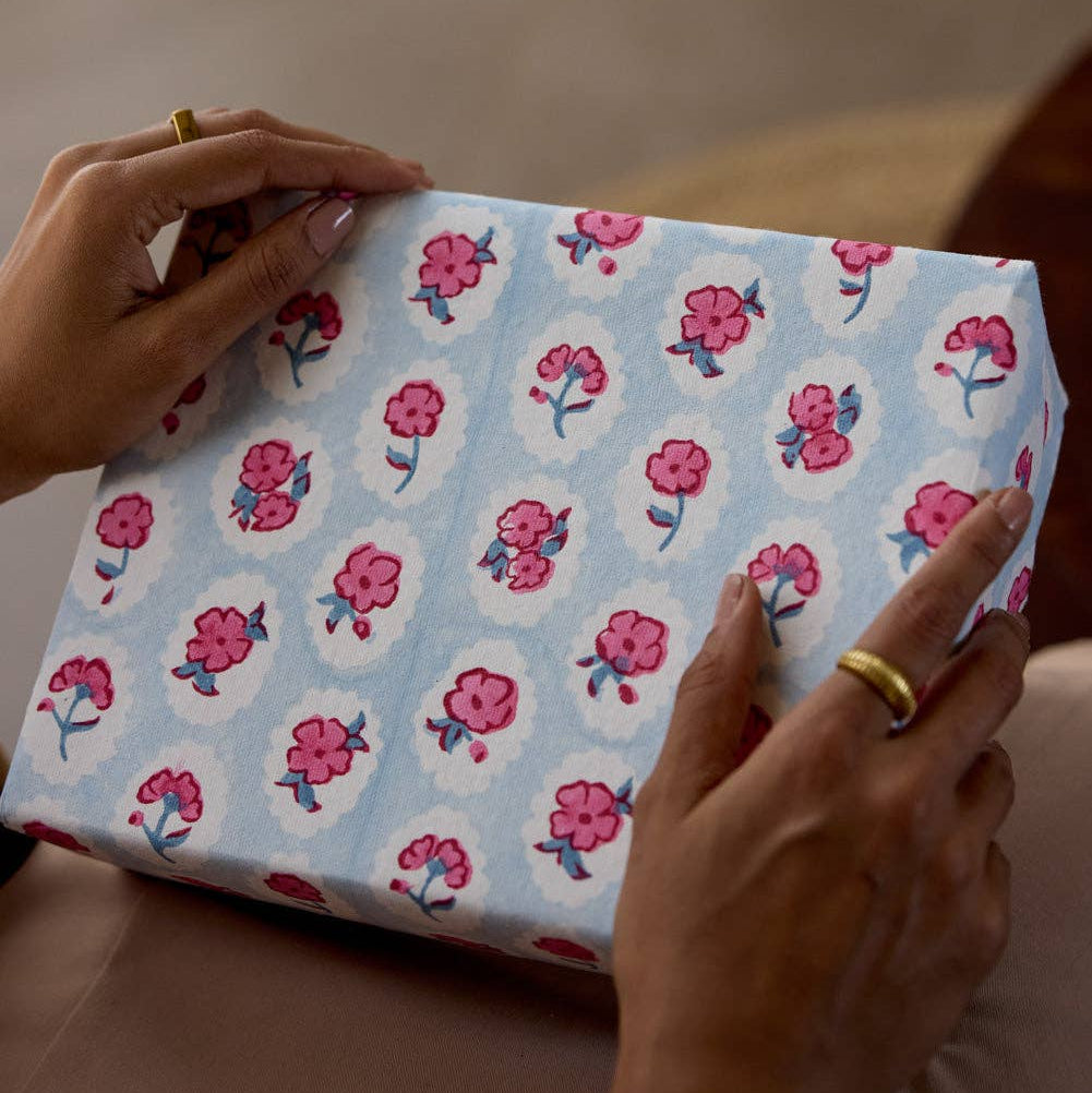 Person holding a gift box with floral pattern on a neutral background