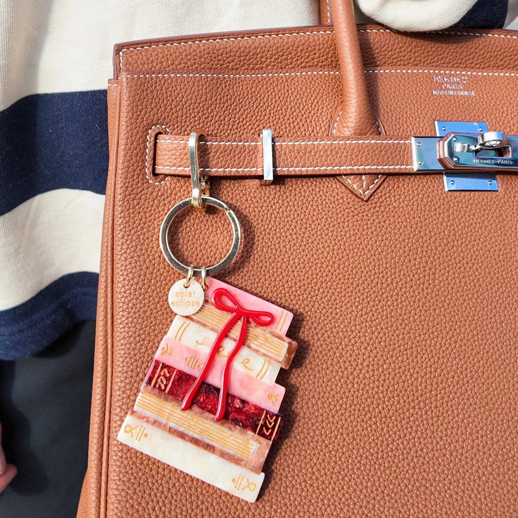 Brown leather handbag with a decorative keychain featuring a cake design and red ribbon.