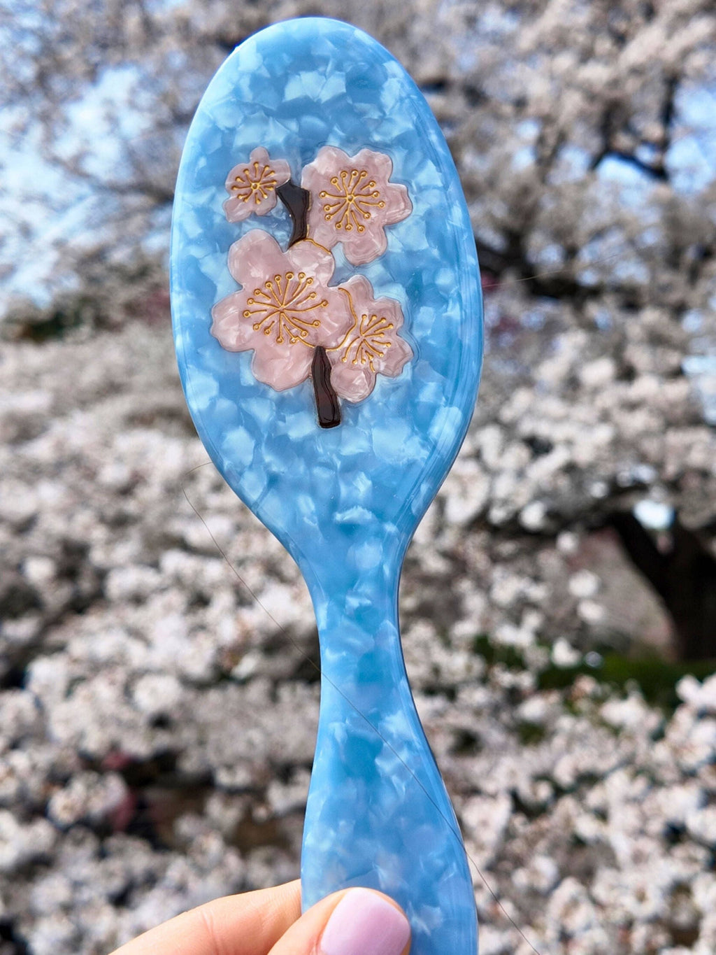 Blue spoon with cherry blossom design held in front of cherry blossom trees
