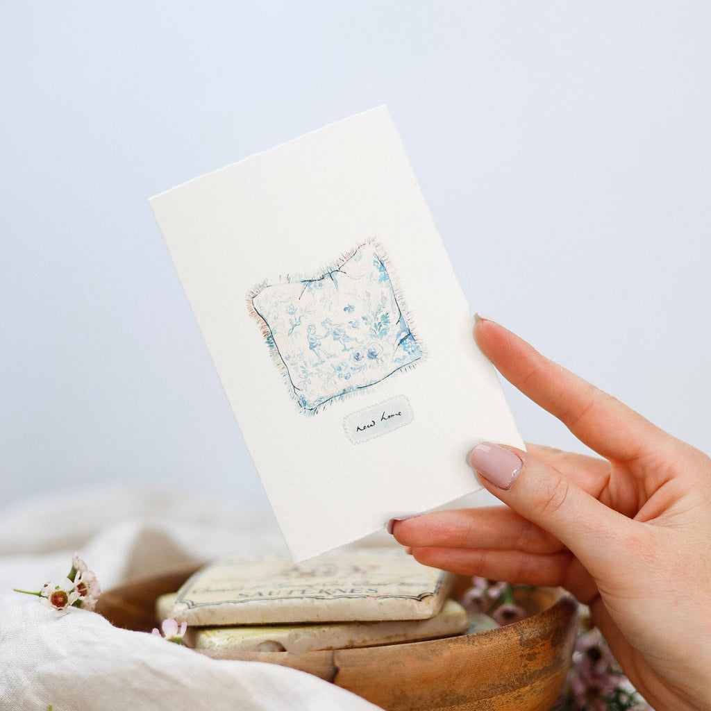 Hand holding a small white box with a floral design on a light background
