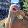 Person with a pink hairbrush with a rose design, standing outdoors with buildings and greenery in the background.