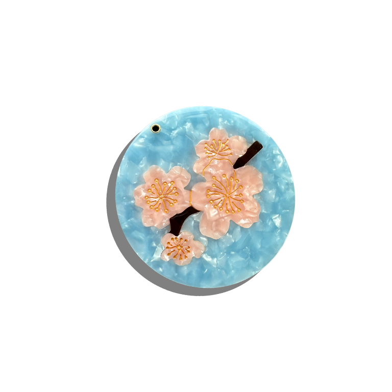 Round blue pendant with pink floral designs on a white background