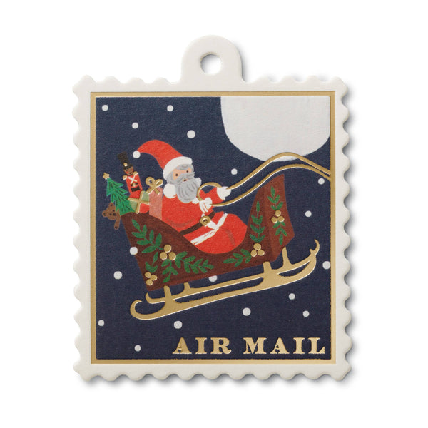 Decorative ornament with Santa Claus in a sleigh, surrounded by Christmas trees and presents, on a blue background with 'Air Mail' text.