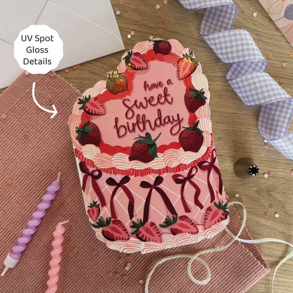 Decorative birthday card with cake design and strawberries on a wooden surface.