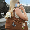 Woman with a brown handbag featuring floral and butterfly charms, talking on a floral phone, with a blurred background.