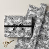 Gift box with black and white pattern and ribbon, surrounded by matching fabric and scissors on a light background