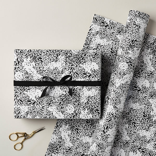 Gift box with black and white pattern and ribbon, surrounded by matching fabric and scissors on a light background