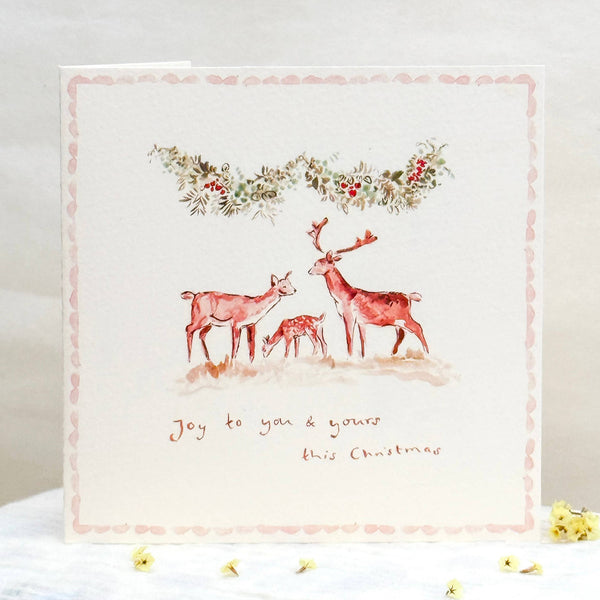 Decorative card with deer illustration and floral wreath on a white surface.