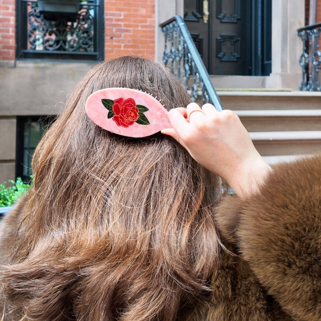 Person adjusting a hair clip with a rose design on their head outdoors.