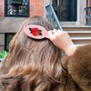 Person adjusting a hair clip with a rose design on their head outdoors.