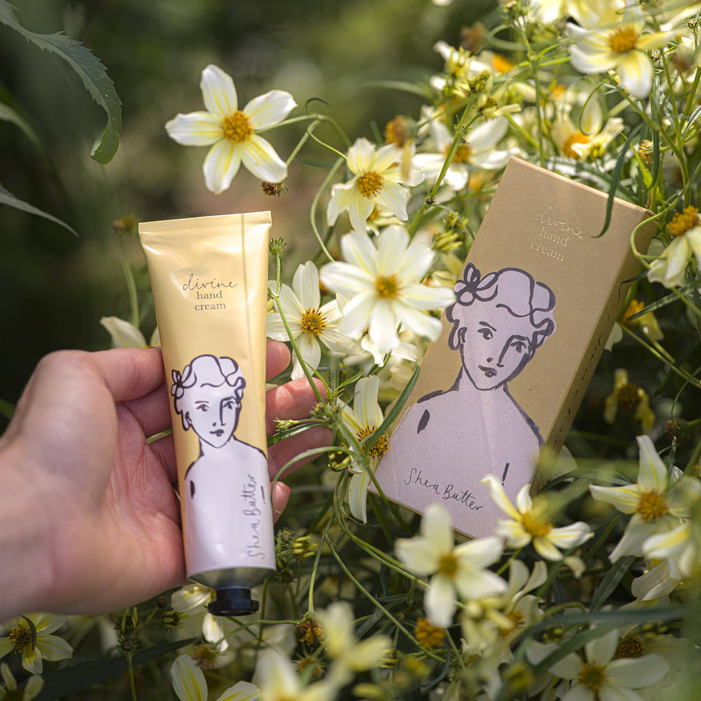 Hand holding a tube of 'Shea Butter' with packaging amidst flowers