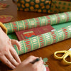 Person wrapping a gift with colorful paper and scissors on a wooden table.