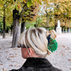 Person with styled hair in an outdoor setting with trees and a path