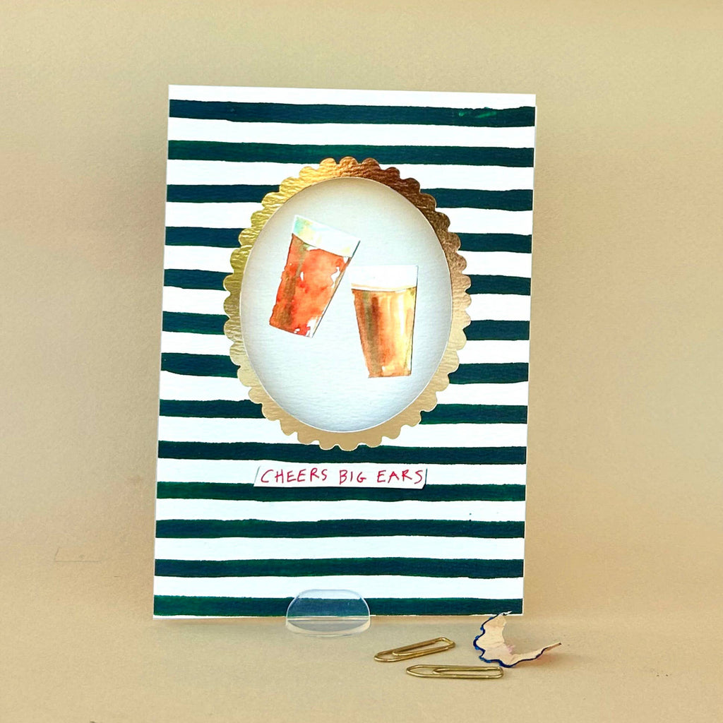 Notebook with striped cover featuring two glasses and 'Cheers Big Ears!' text on a beige background