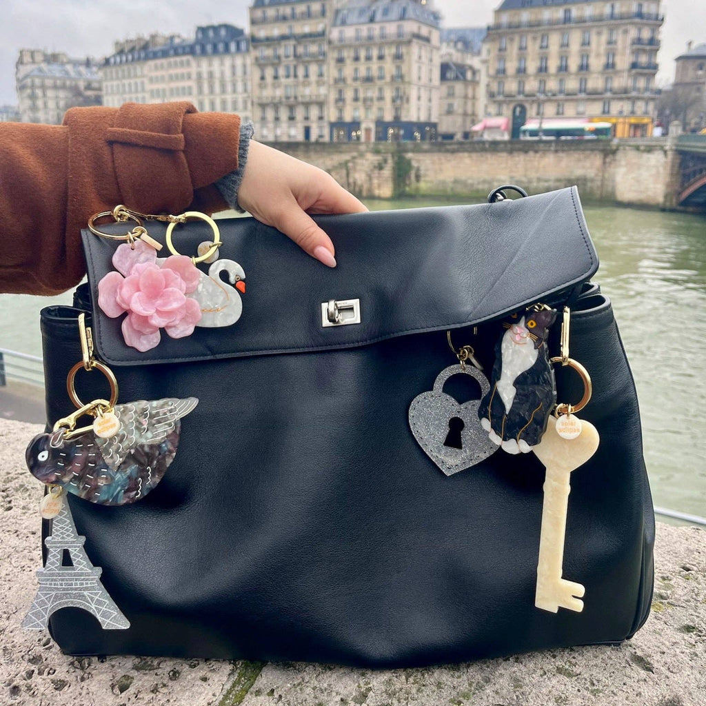 Black handbag with decorative charms held by a person in an urban setting.