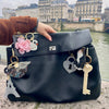 Black handbag with decorative charms held by a person in an urban setting.