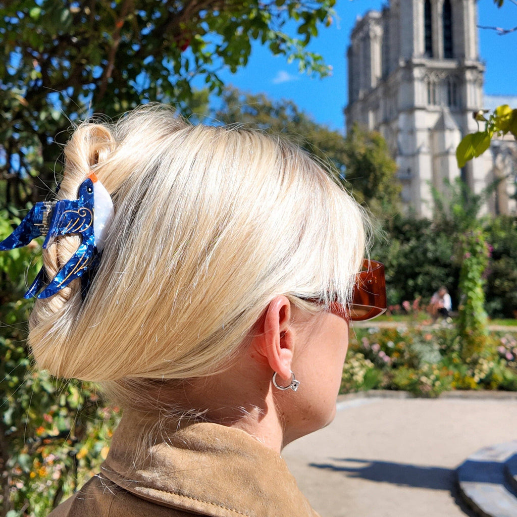 Person with blonde hair and a blue hair accessory, looking towards a cathedral.