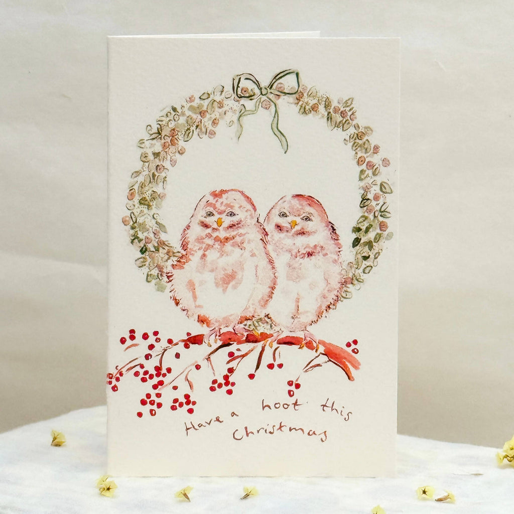 Christmas card with two birds and a wreath on a white surface.