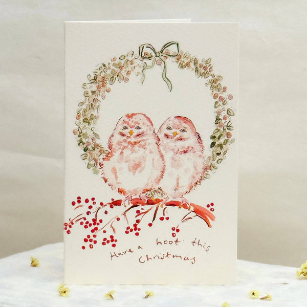 Christmas card with two birds and a wreath on a white surface.