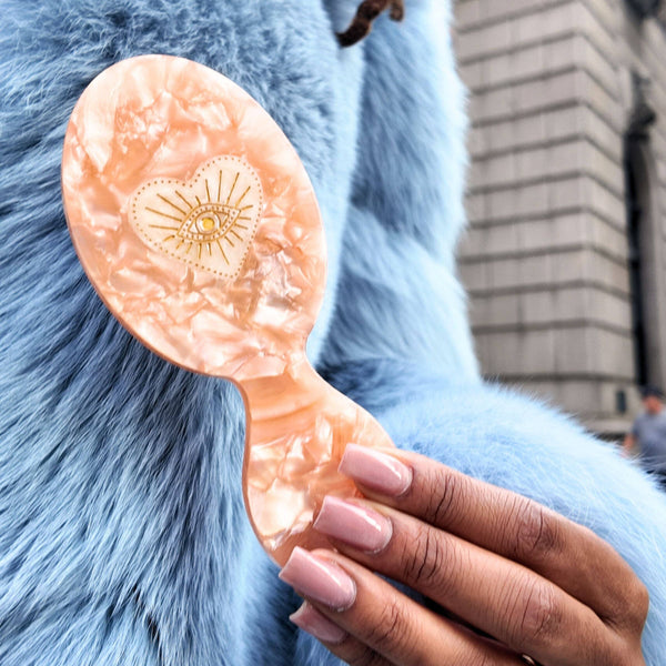 Person holding a pink hairbrush with a shell design against a blue fur background